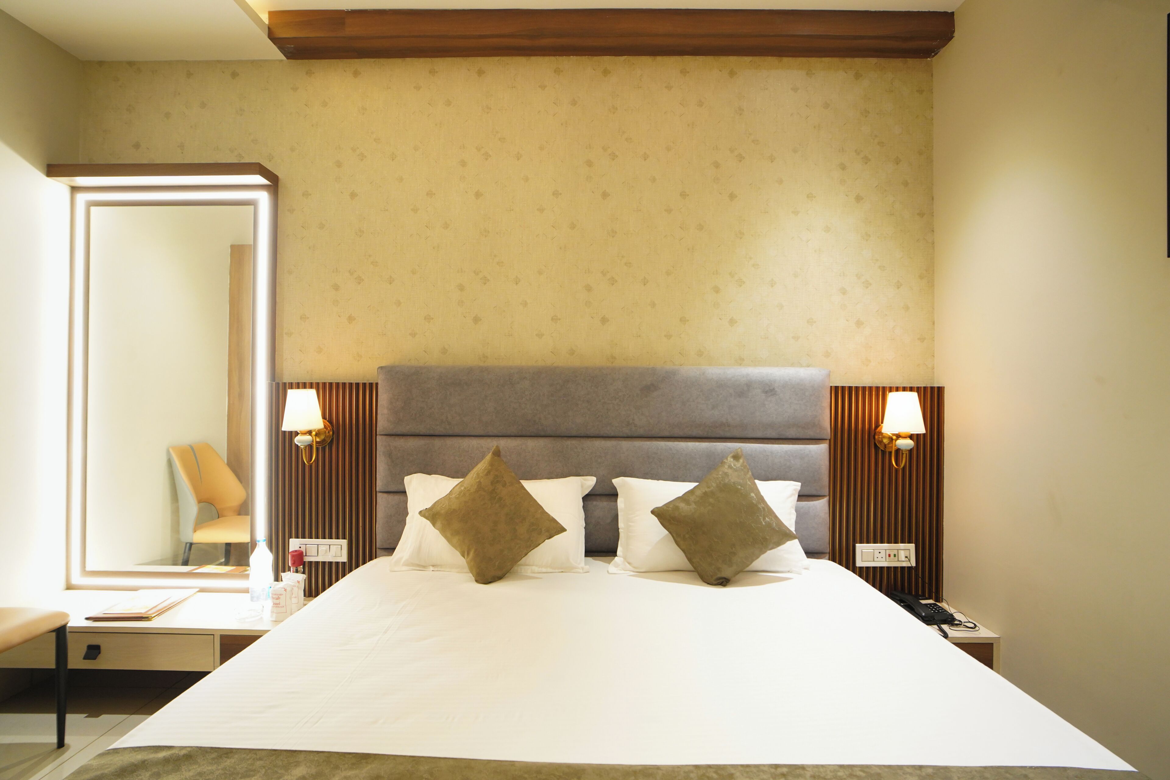 Ein Hotelzimmer mit einem großen Bett, zwei Nachttischlampen, einem Nachttisch mit Telefon und einem Spiegel, der einen Sessel reflektiert.