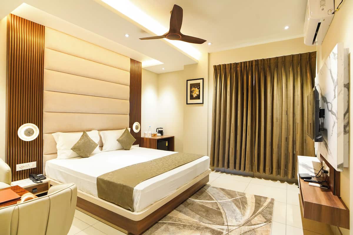 A hotel room with a large bed, a desk with a chair, a ceiling fan, a TV, and a window with curtains.