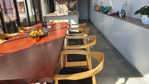 A modern kitchen with a long wooden table and chairs, a fruit basket, and a countertop with various items.