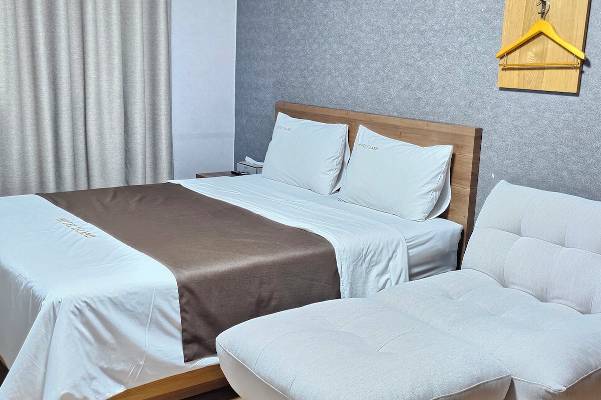 A neatly arranged hotel room with a bed, a bedside table, and a sofa.