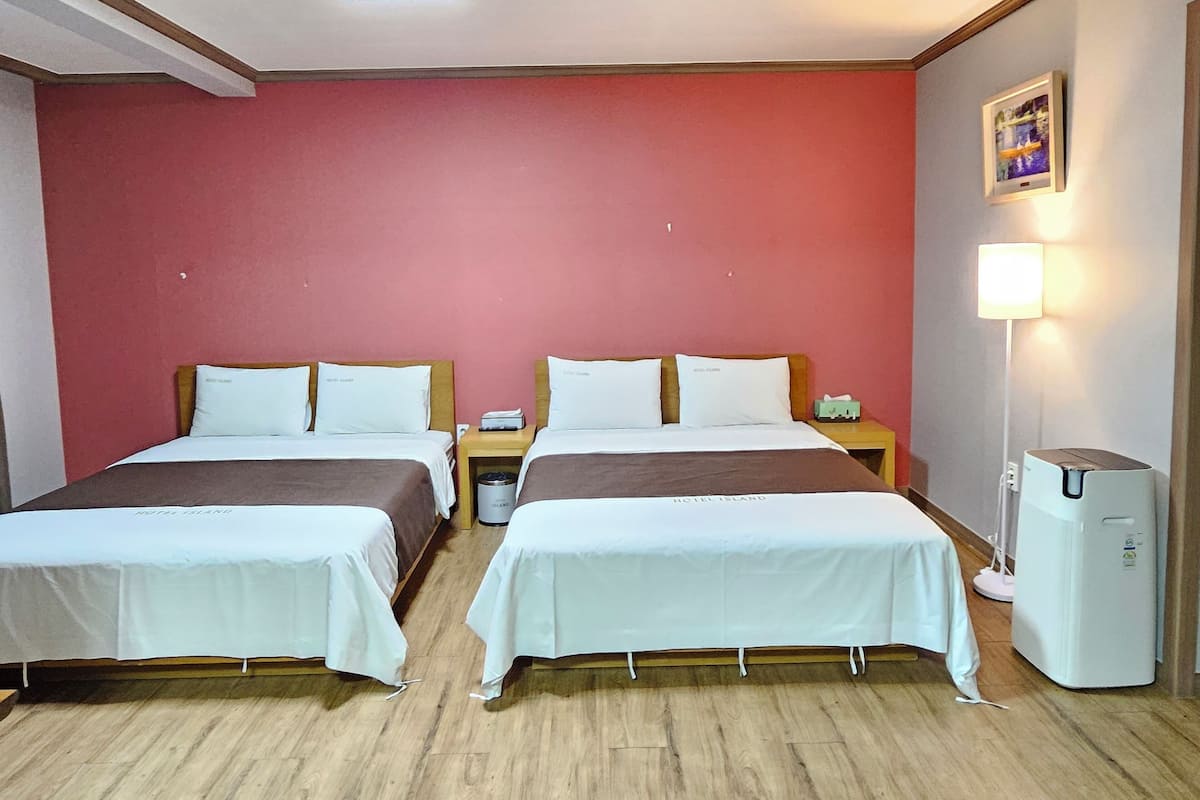 A hotel room with two beds, a nightstand, a trash bin, a heater, and a wall-mounted lamp.