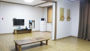 Una habitación con un banco de madera, televisión, microondas, refrigerador y una puerta que da a otra habitación.
