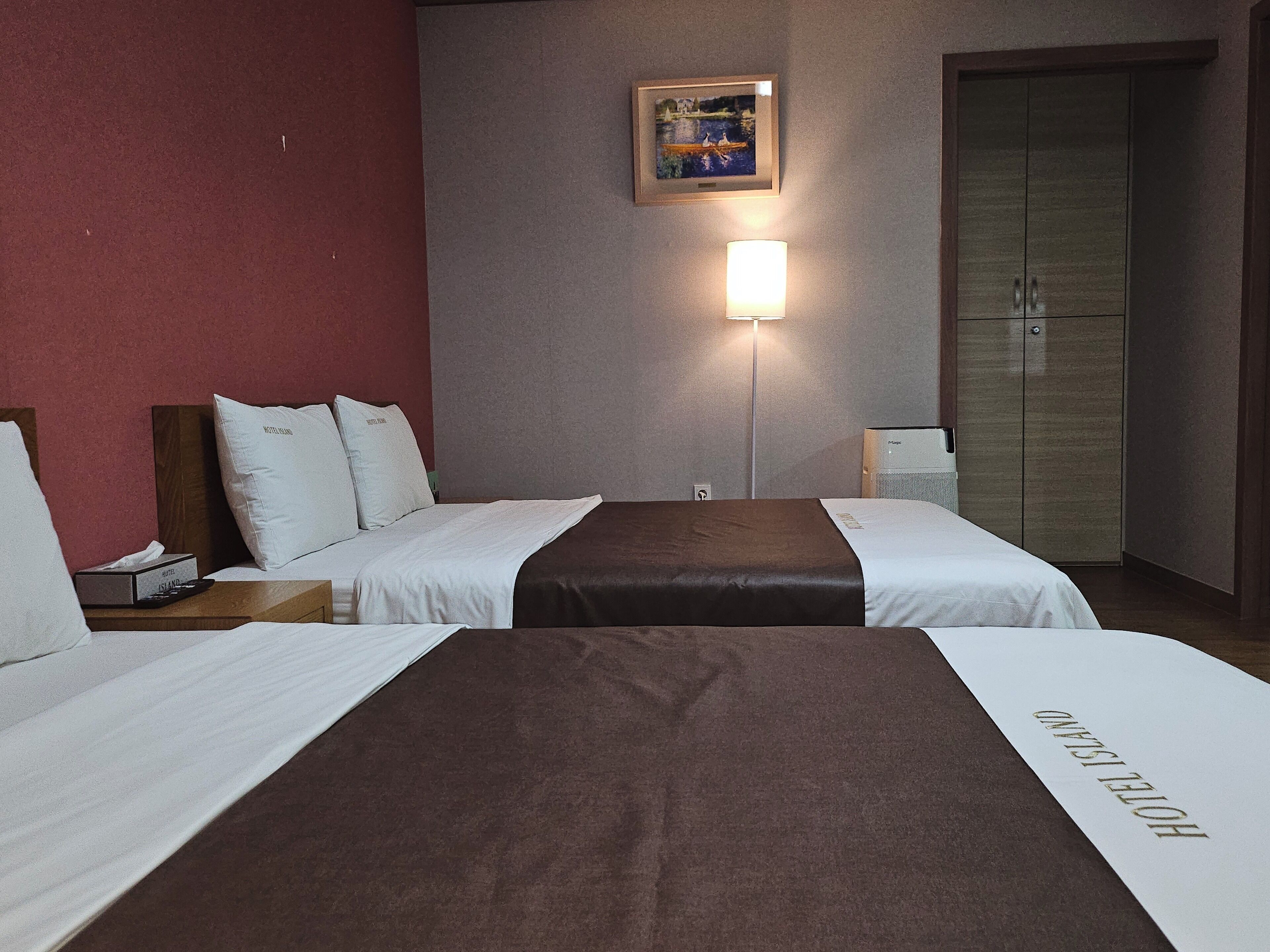 Habitación de hotel con dos camas, una mesita de noche, una lámpara, un armario y un cuadro en la pared.