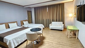 Una habitación de hotel con dos camas, un sofá, una mesita redonda y un televisor montado en la pared.