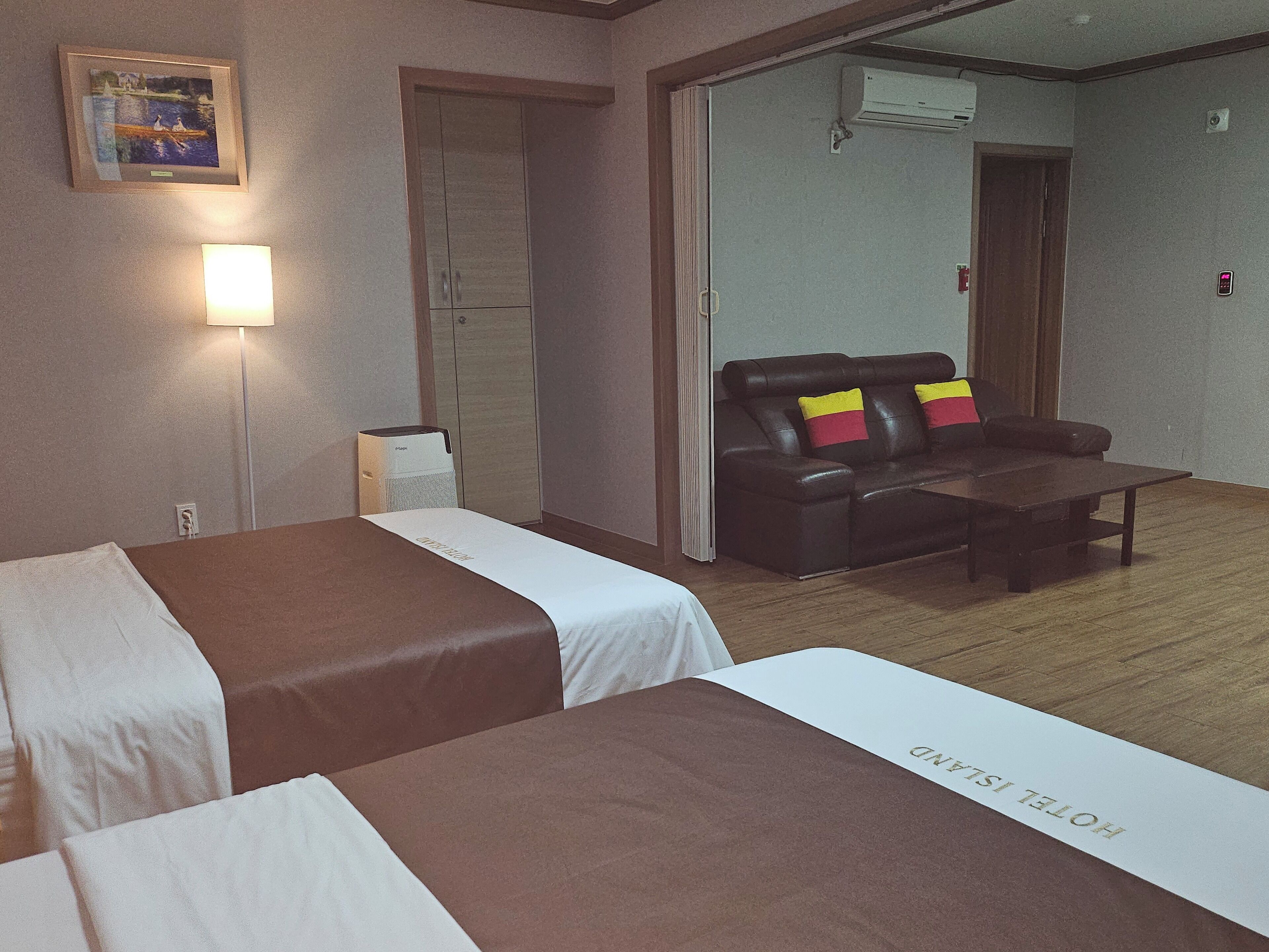 Une chambre d’hôtel avec deux lits, un canapé, une table basse, une lampe et un appareil de climatisation.