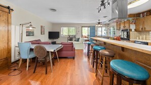 A modern kitchen with wooden cabinets, a central island with stools, and a dining area with a table and chairs.