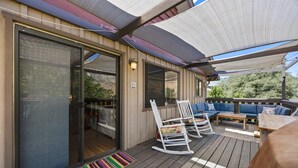 A covered outdoor deck with a seating area, a rocking chair, and a table.