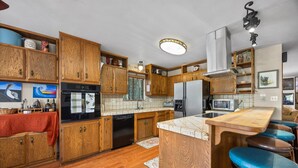 A kitchen with wooden cabinets, a dishwasher, a refrigerator, a microwave, and a bar area with stools.