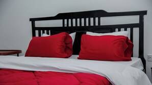 Una cama con cabecera negra, ropa de cama blanca y almohadas rojas.