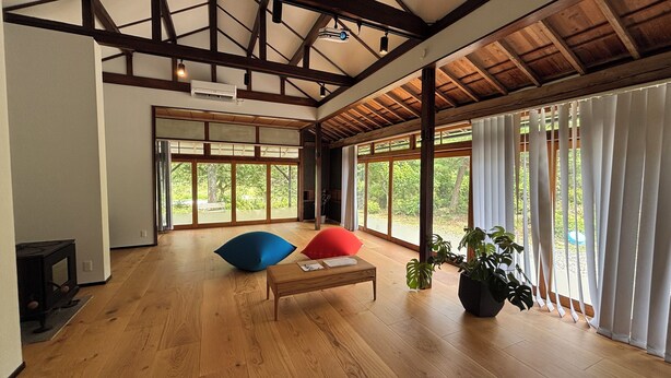 A spacious room with wooden floors, a wooden ceiling, and large windows with white curtains.