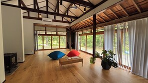 Une pièce spacieuse dotée de planchers en bois, d’un plafond en bois et de grandes fenêtres ornées de rideaux blancs.