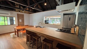 A modern kitchen with a central island, wooden chairs, a sink, and a window overlooking greenery.
