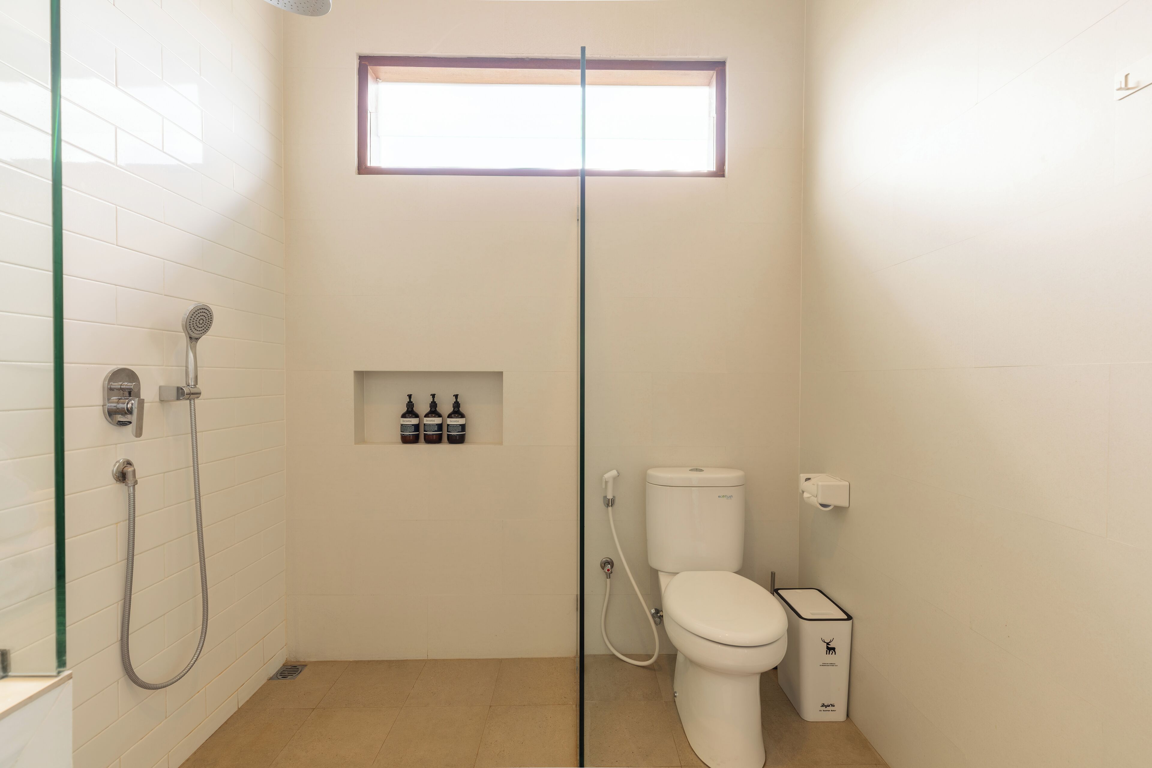 A bathroom with a glass shower enclosure, a toilet, and a window above the shower.