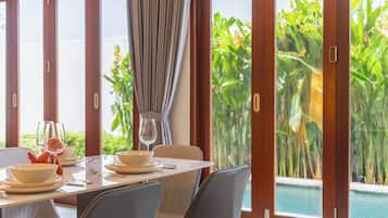 A dining area with a table set for four, large windows, and a view of a swimming pool and greenery.
