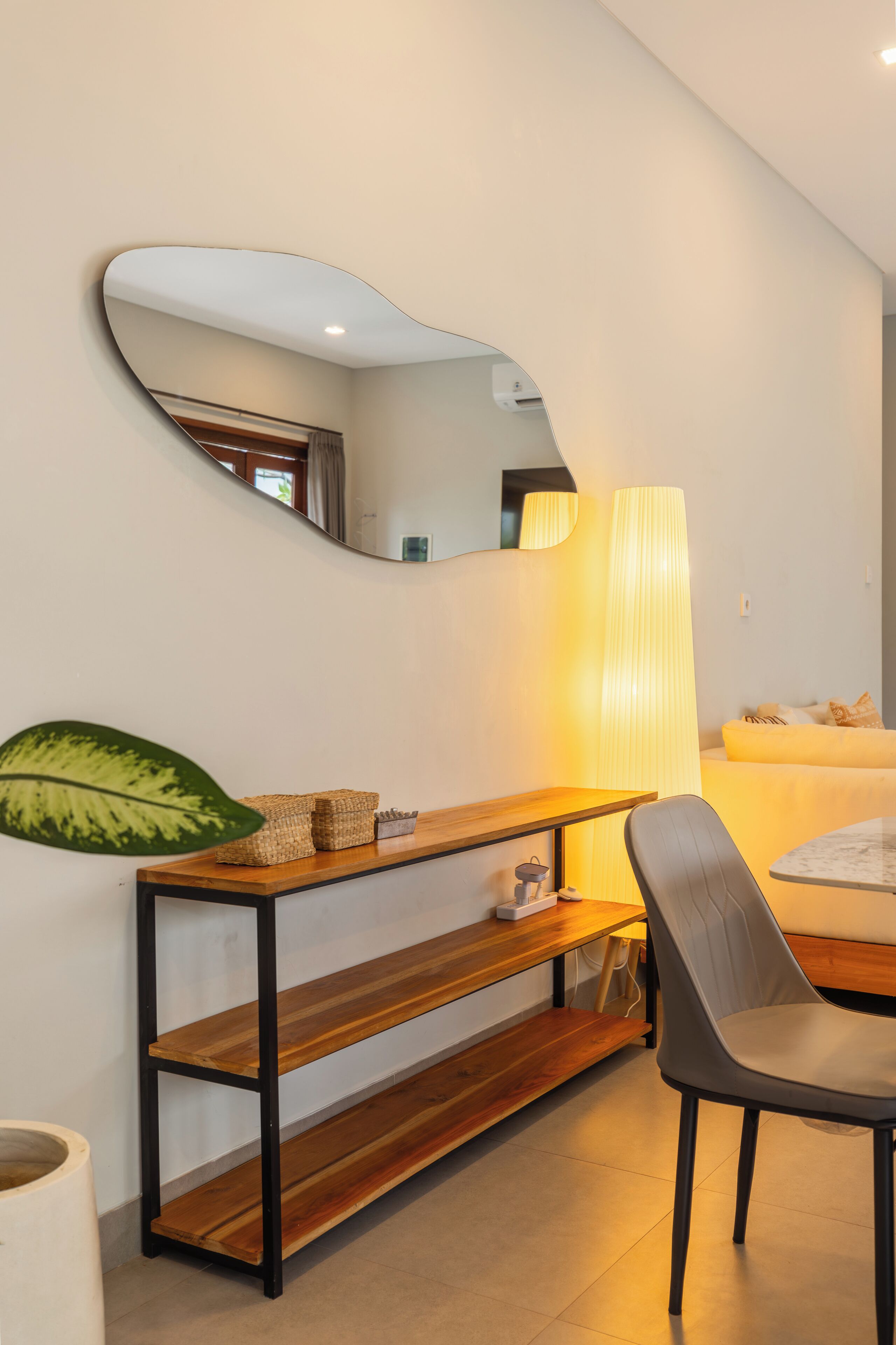 A modern living room with a wooden console table, a mirror, a lamp, and a chair.