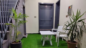 A small room with artificial green carpet, a white table, two white chairs, and two potted plants.