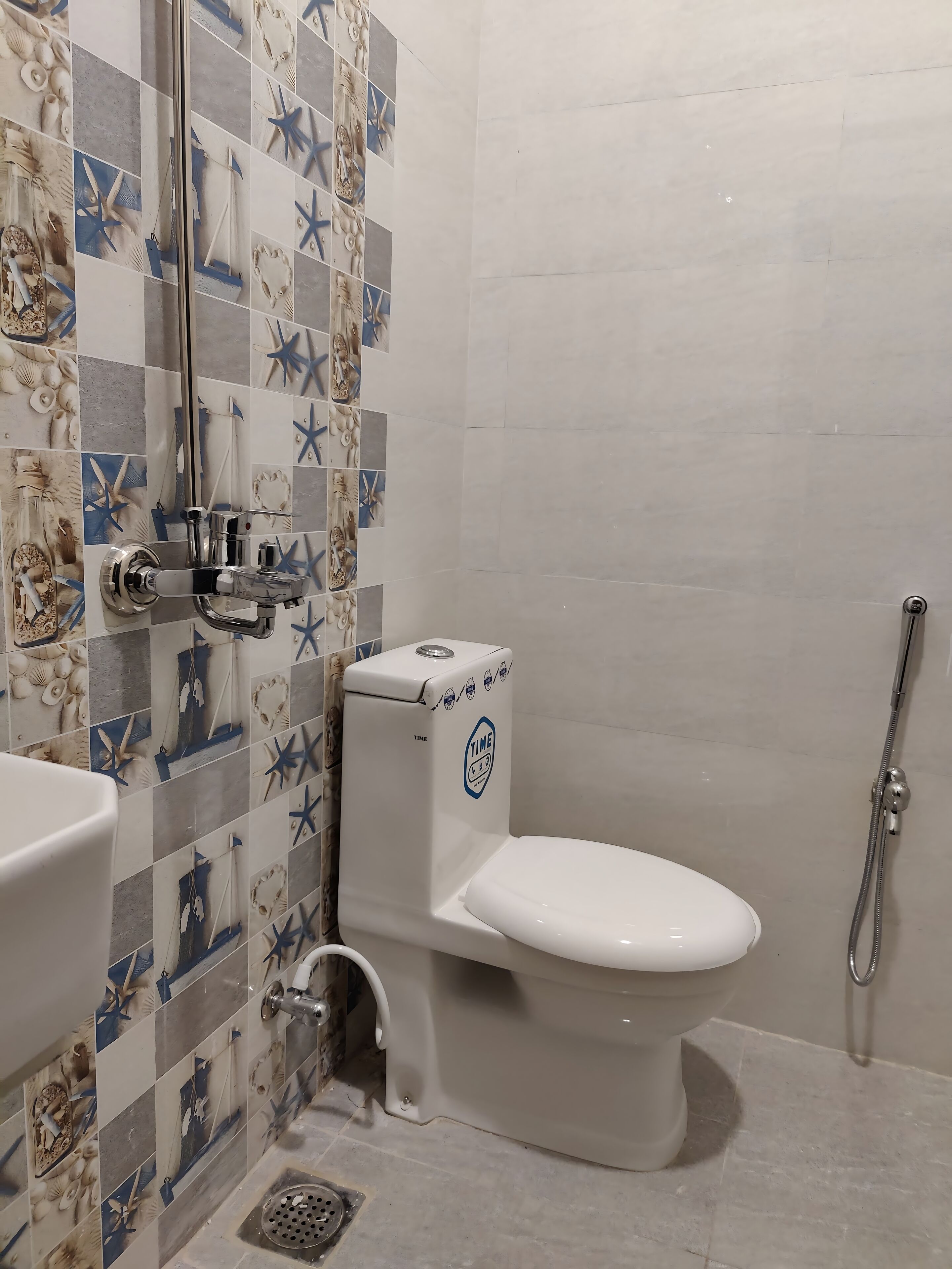 Ein Badezimmer mit Toilette, Dusche und Fliesenwänden, verziert mit Meeresschnecken und Meeressternen.