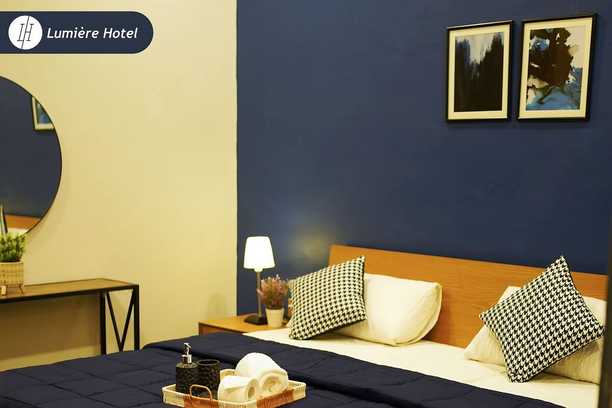 Une chambre d’hôtel comprenant un lit, une table de chevet, une lampe et un plateau avec des articles de toilette.