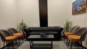 A modern living room with a black leather sofa, four armchairs, a coffee table, and two potted plants.