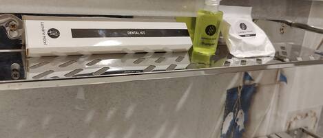 A bathroom with a dental kit, shampoo, and conditioner on a shelf.