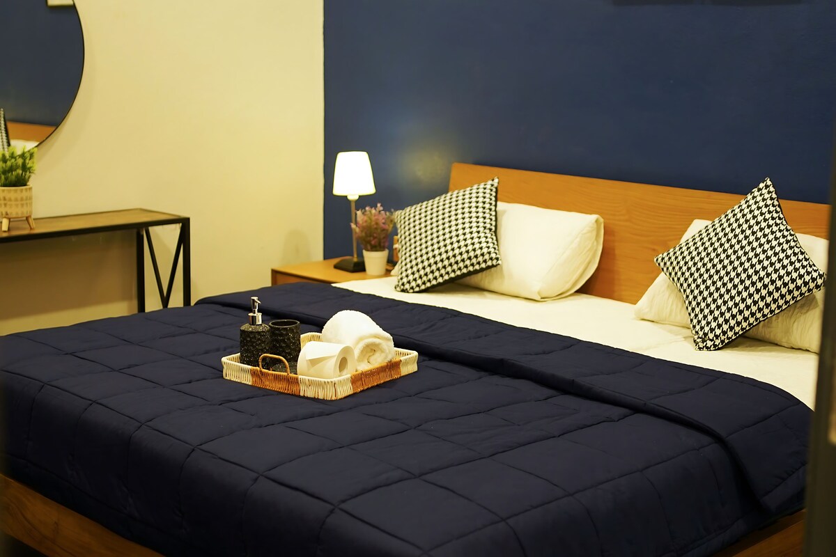Ein Hotelzimmer mit Bett, Nachttisch, Lampe und Tablett mit Toilettenartikeln.