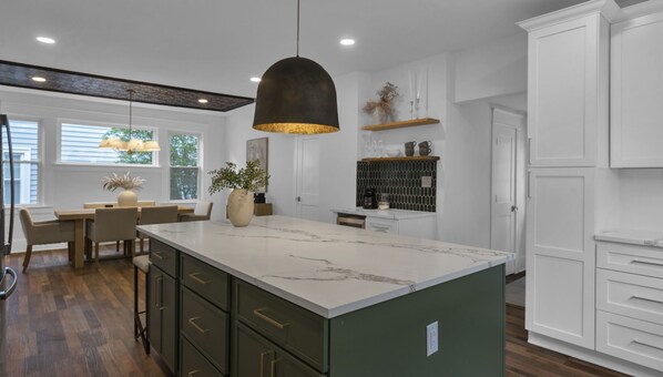 A modern kitchen with a large island, green cabinets, white countertops, and pendant lighting. - Downtown, Historic, Newly Renovated (Raleigh)