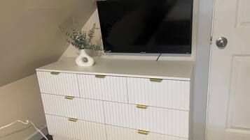A white dresser with gold handles, a black TV on top, and a small white vase with a plant.