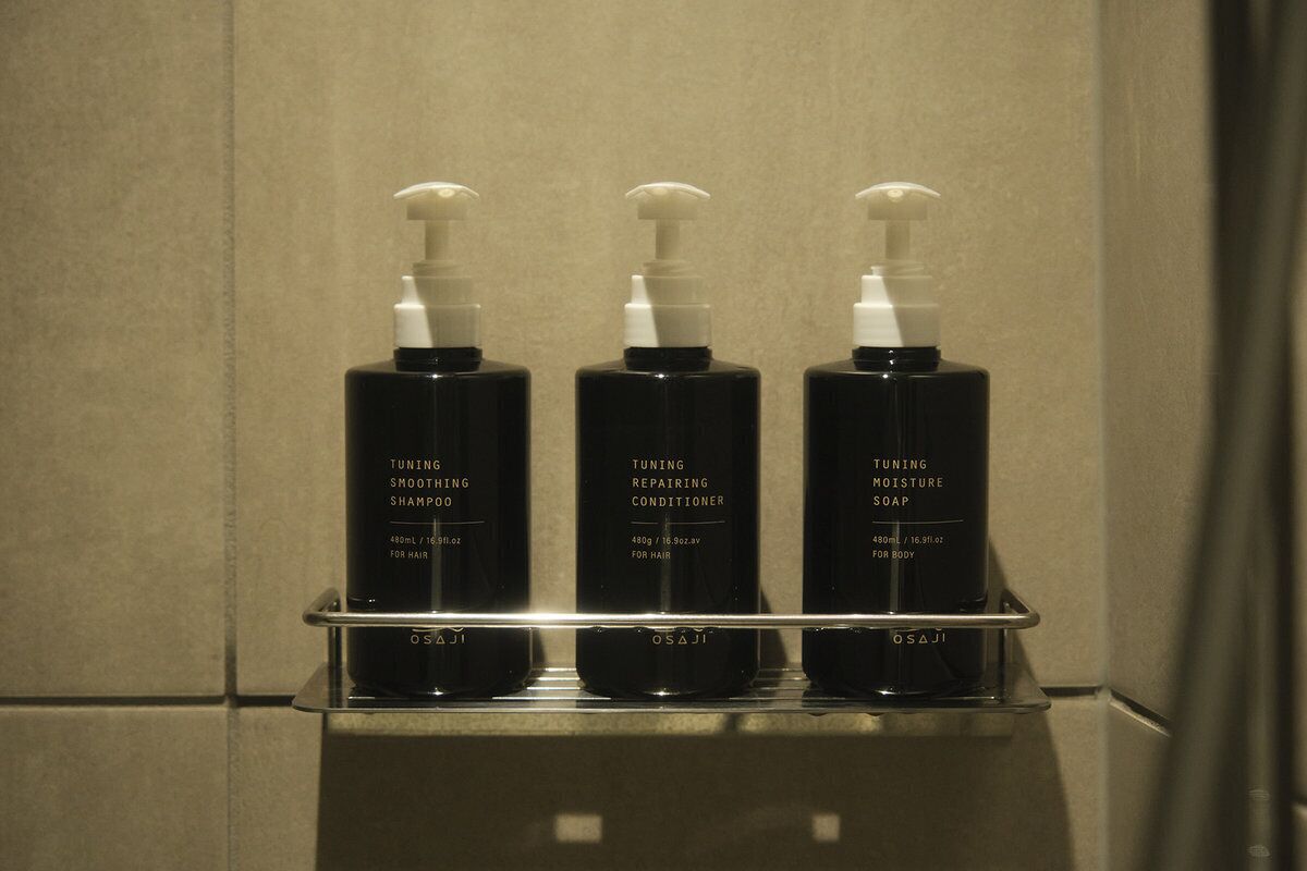 Trois flacons noirs de produits de soins pour les cheveux et le corps de la marque Osajii, posés sur une étagère dans une salle de bain.