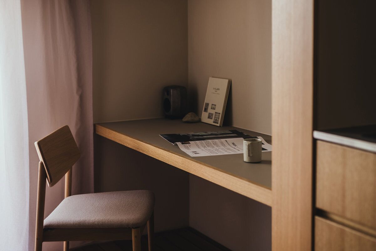 Een hoek van een kamer met een houten bureau, een stoel en een lijst met een afbeelding aan de muur.