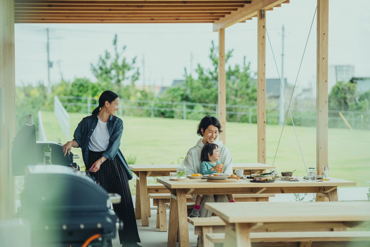 A covered outdoor dining area with wooden tables and benches, a person standing near a table, and another person seated at a table.