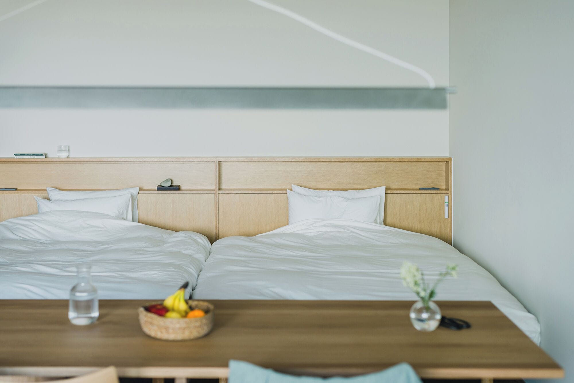 A double bed with a wooden headboard, a bedside table with a fruit bowl and a vase, and a bedside lamp.