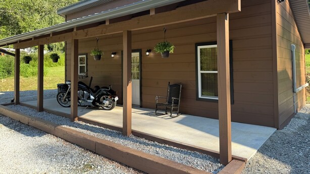 Ein Holzhaus mit überdachter Veranda, einem draußen abgestellten Motorrad und hängenden Pflanzen.