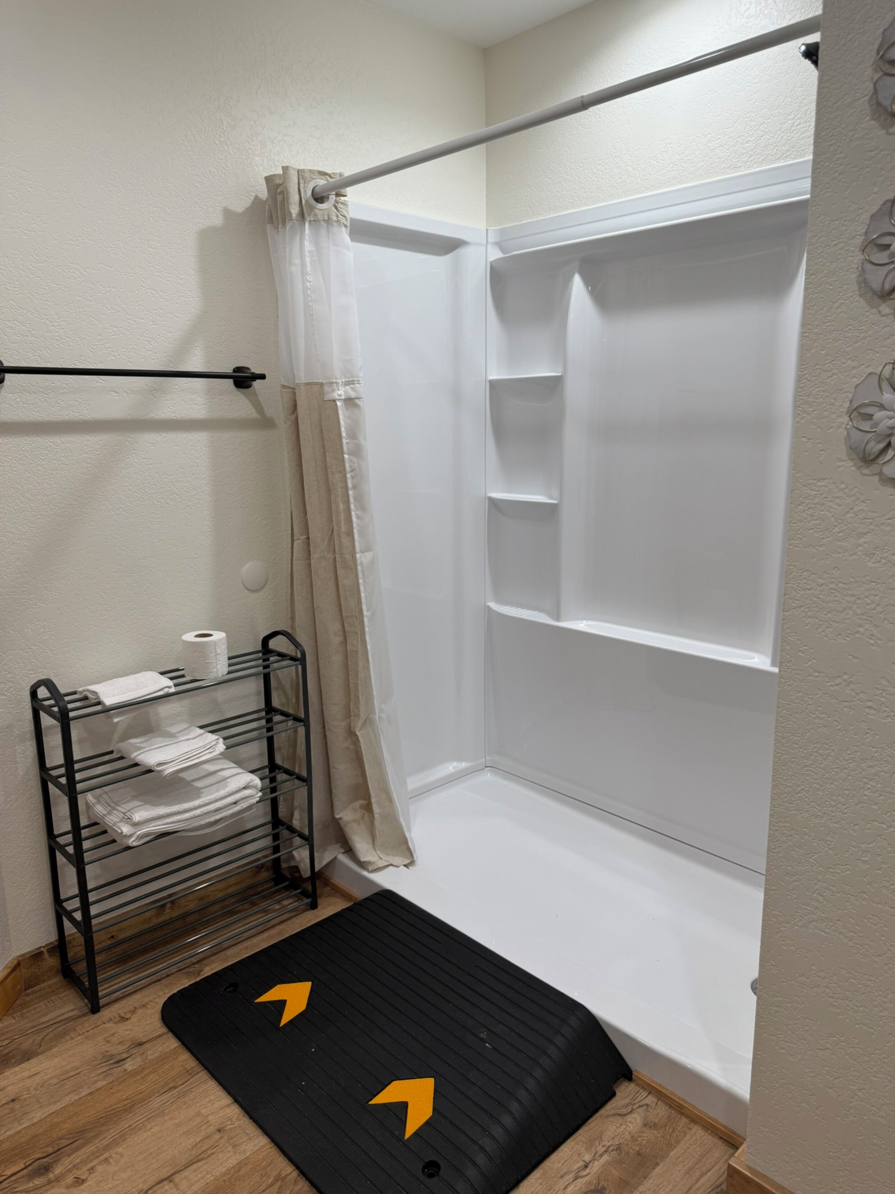 Un espace douche doté d’une étagère en verre pour ranger les serviettes et d’un tapis noir orné de flèches indiquant le sens.