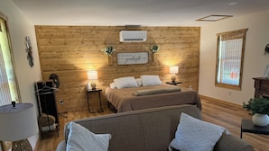 Ein gemütliches Zimmer mit Holzwand, einem Bett, einer Couch und einem kleinen Tisch mit Lampe.