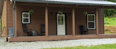 A single-story house with a covered porch, a front door, and two windows.
