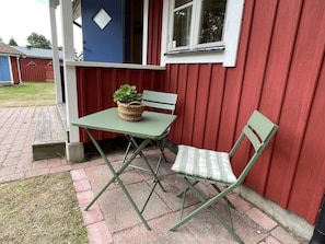 A small outdoor seating area with a table and two chairs, a wicker basket with plants, and a red building with a window and a door. - 4 Star Holiday Home in Solvesborg (Sölvesborg)