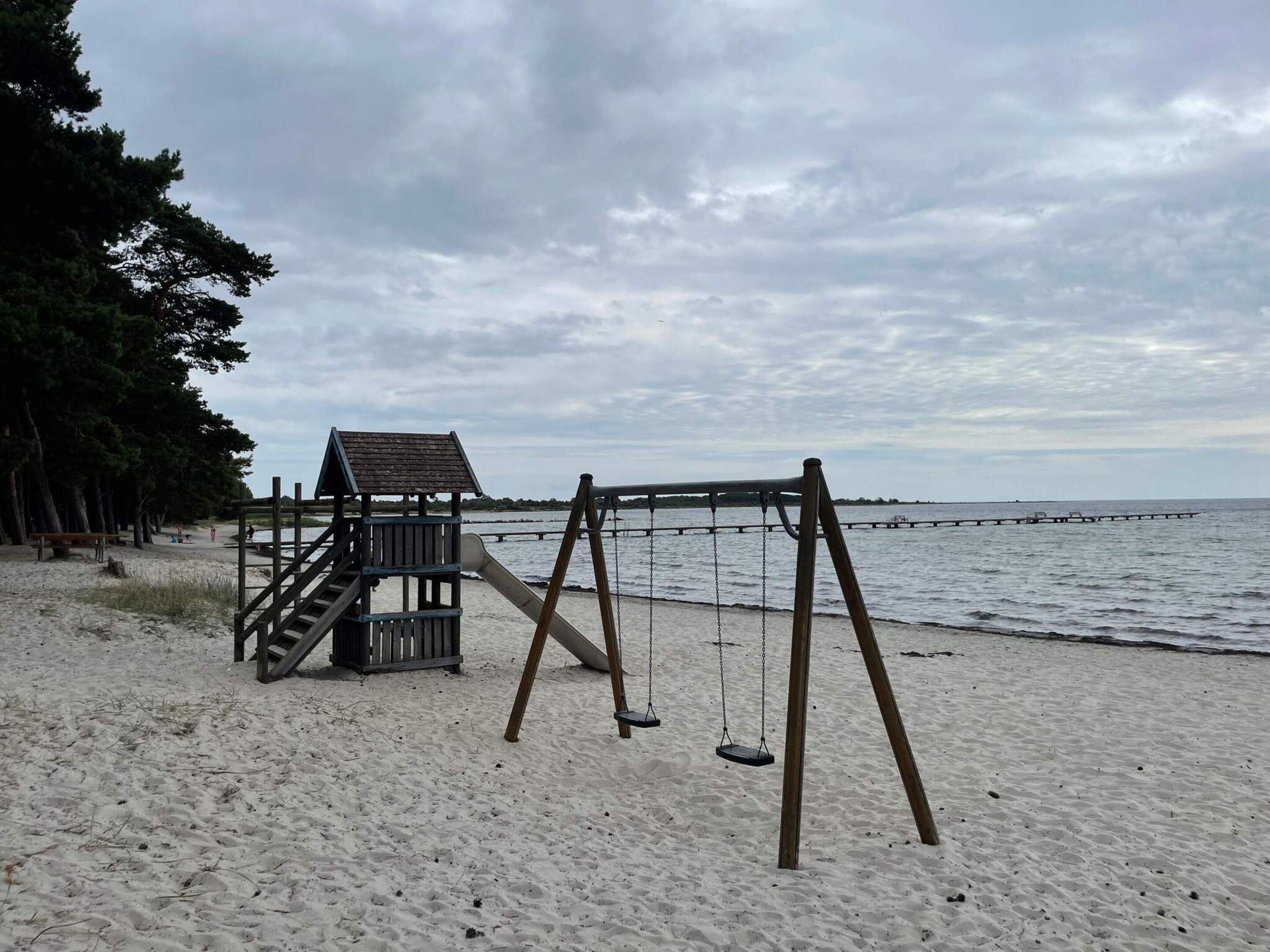 Ein Strand mit einer Holzschaukel und einem kleinen Spielhäuschen.