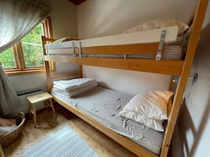 Een slaapkamer met een stapelbed, een tafeltje en een raam.