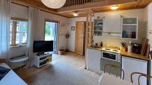 Ein gemütliches Blockhauss-Interieur mit Fernseher, Küchenzeile, Holzboden und einem großen Fenster.