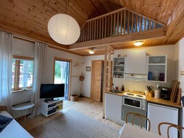 Un interno accogliente di una baita con TV, angolo cottura, soffitto in legno e un'ampia finestra.