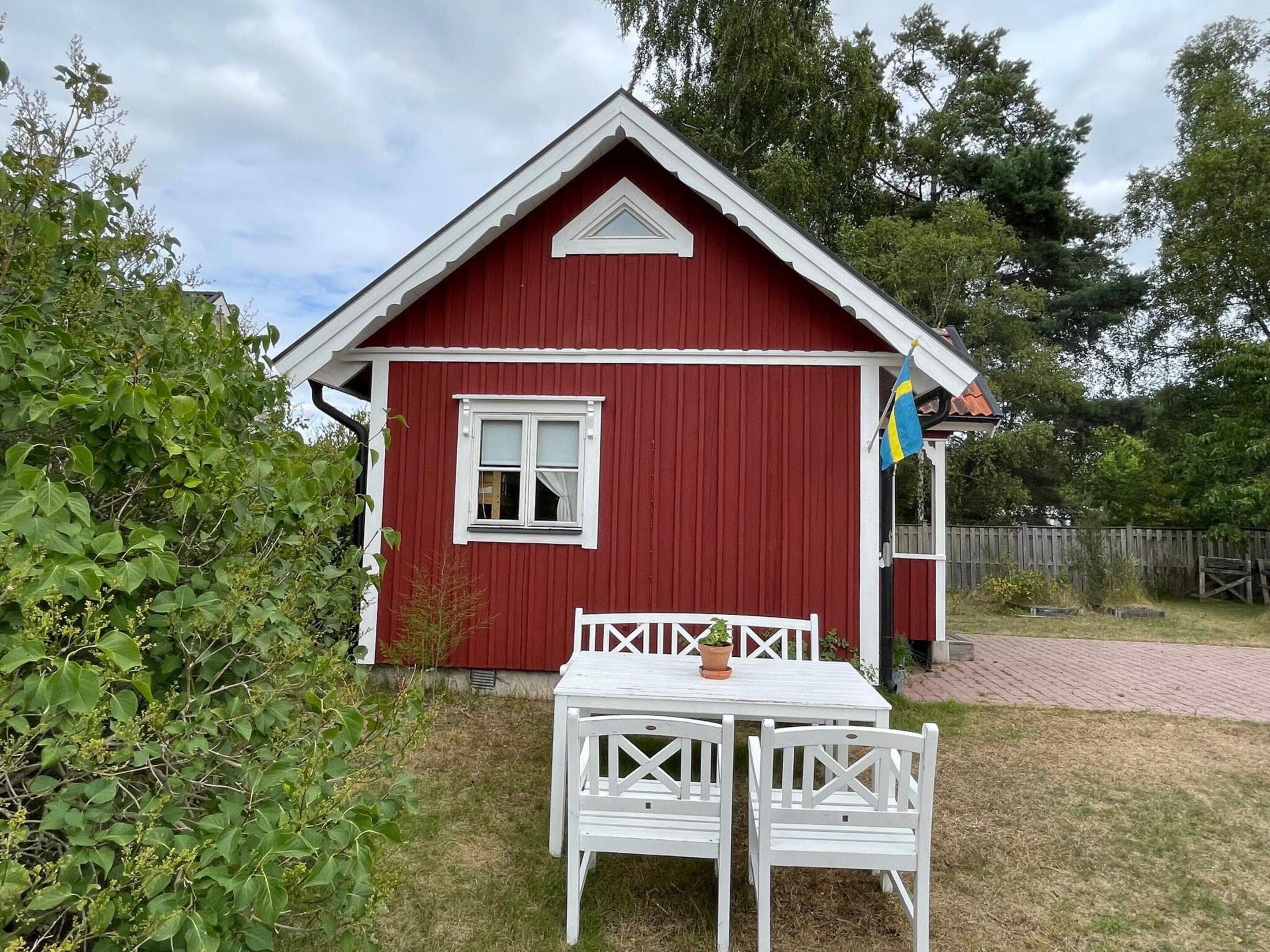 Punainen puutalo, jossa on valkoinen ovi ja ikkuna, pieni kuisti ja pöytä sekä kaksi tuolia sen edessä.
