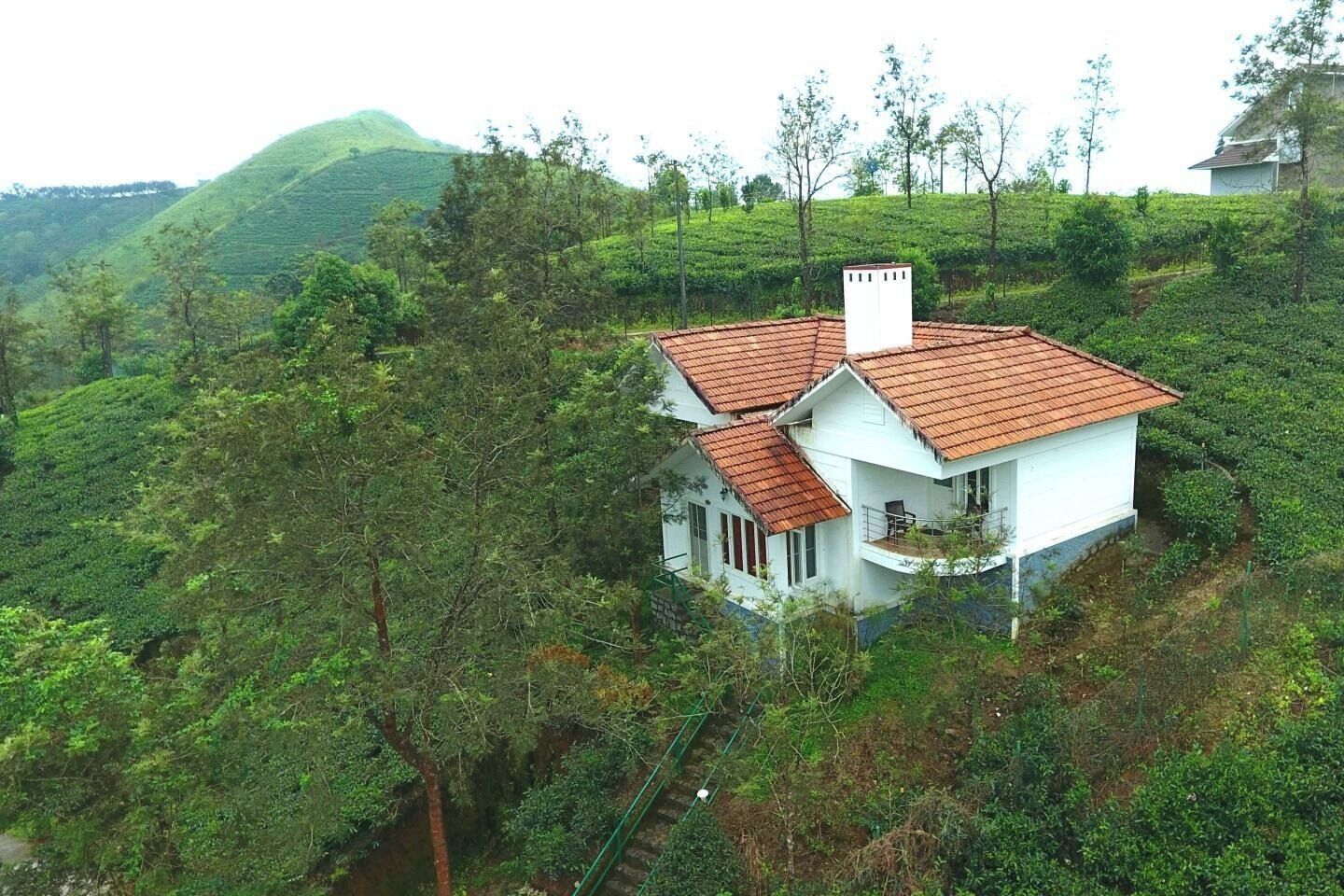 A white house with a red-tiled roof, surrounded by lush greenery and hills.