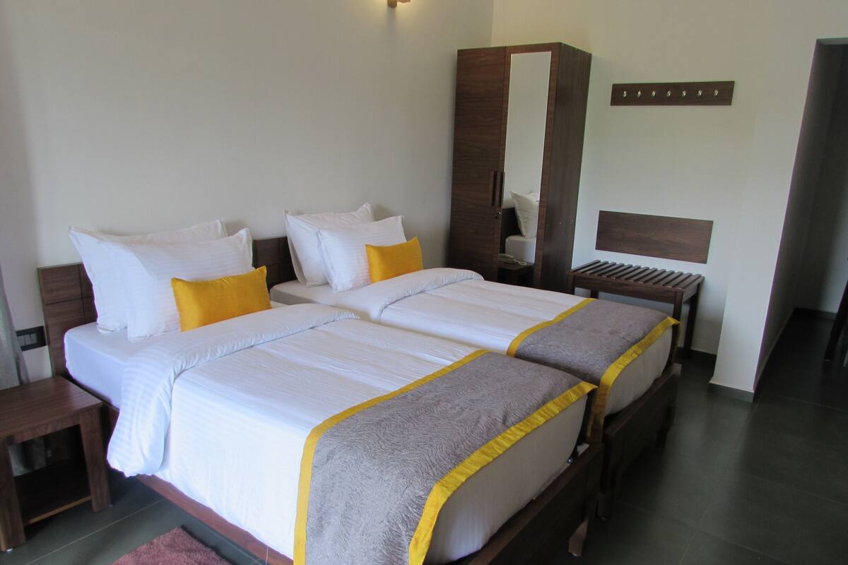 A double bed with white bedding and a grey accent, a wooden wardrobe, and a bedside table with a lamp.