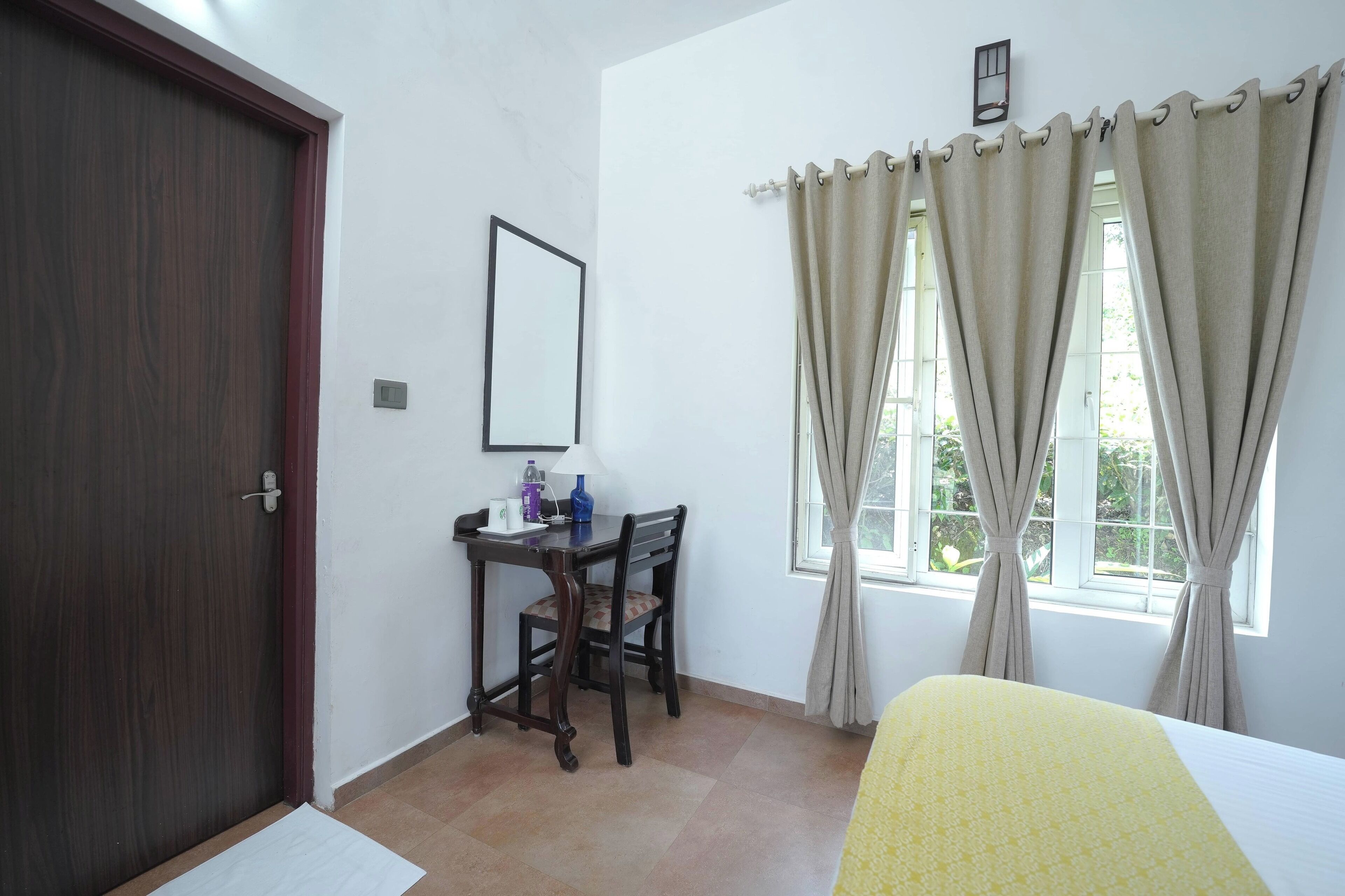 Una habitación con cama, un escritorio y una silla, una ventana con cortinas y una puerta.