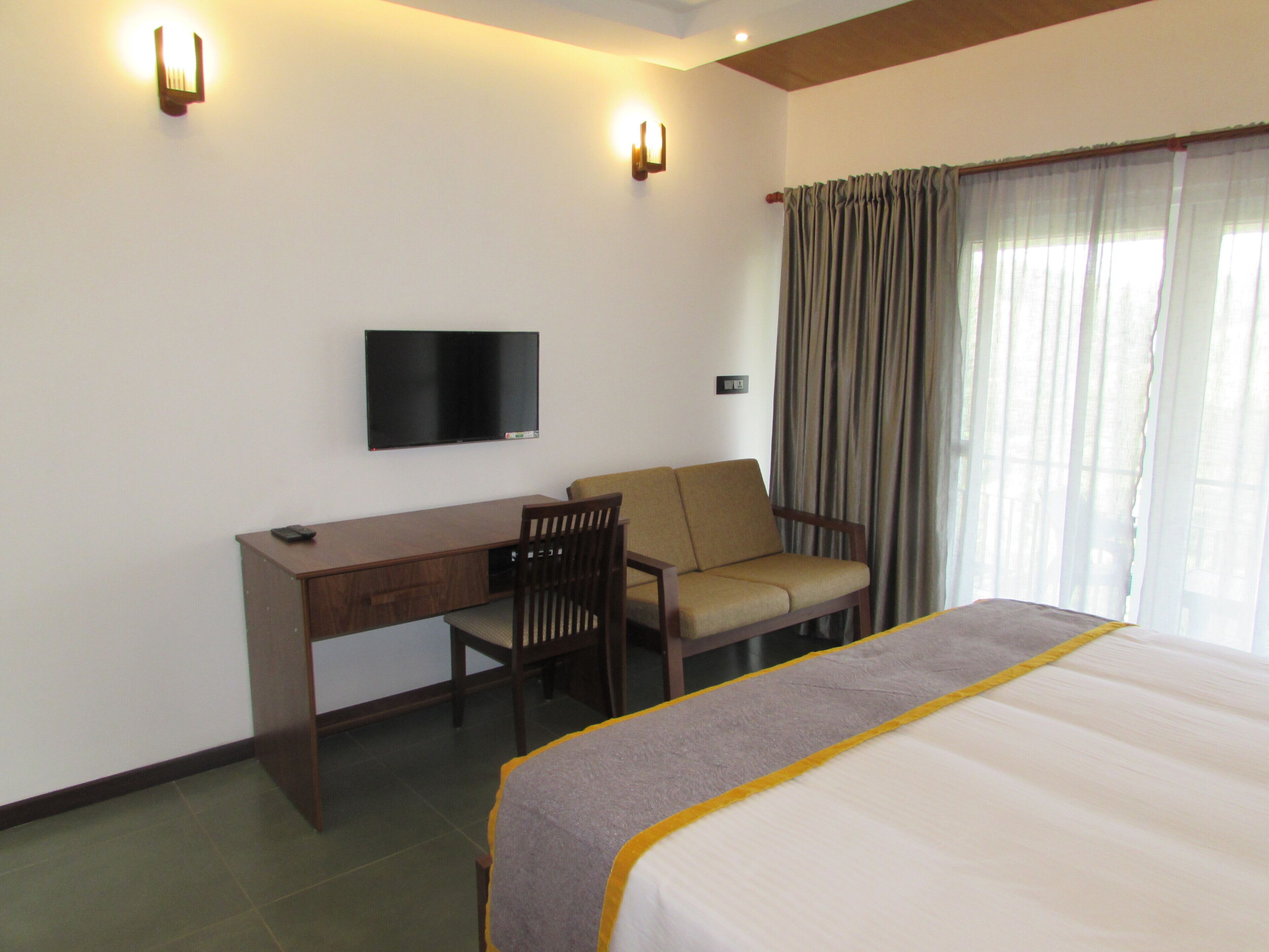 A hotel room with a bed, a desk, a chair, a television, and a window with curtains.