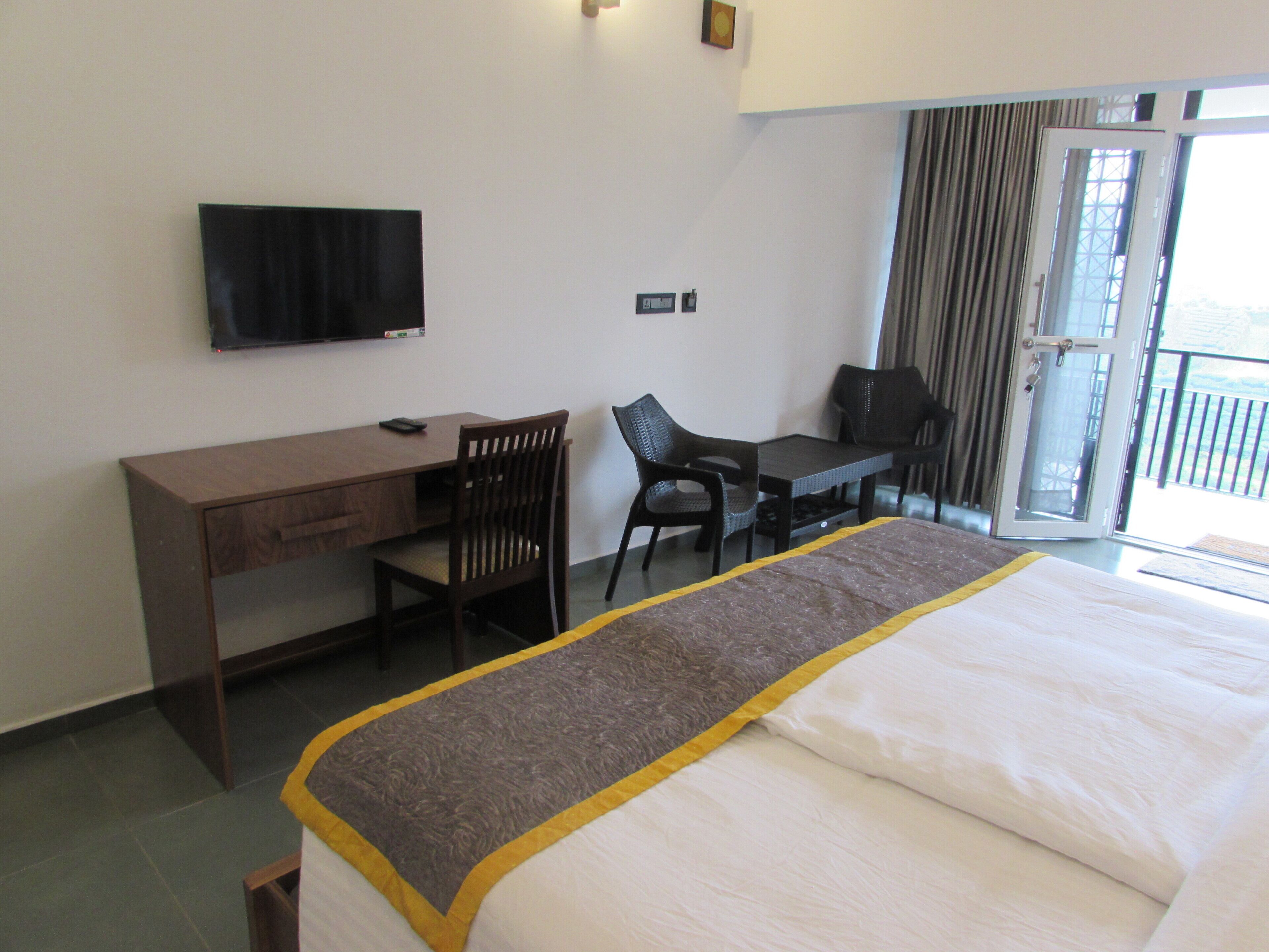 Une chambre d’hôtel comprenant un lit, un bureau avec une chaise, un téléviseur fixé au mur et un balcon avec des rideaux.