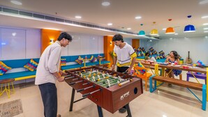 A brightly lit room with a foosball table, colorful seating, and a table with drinks and snacks. - goSTOPS Bengaluru Jayanagar (Bengaluru)