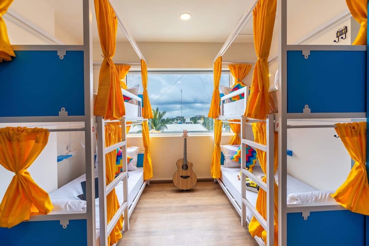A corridor with bunk beds, yellow curtains, and a guitar.