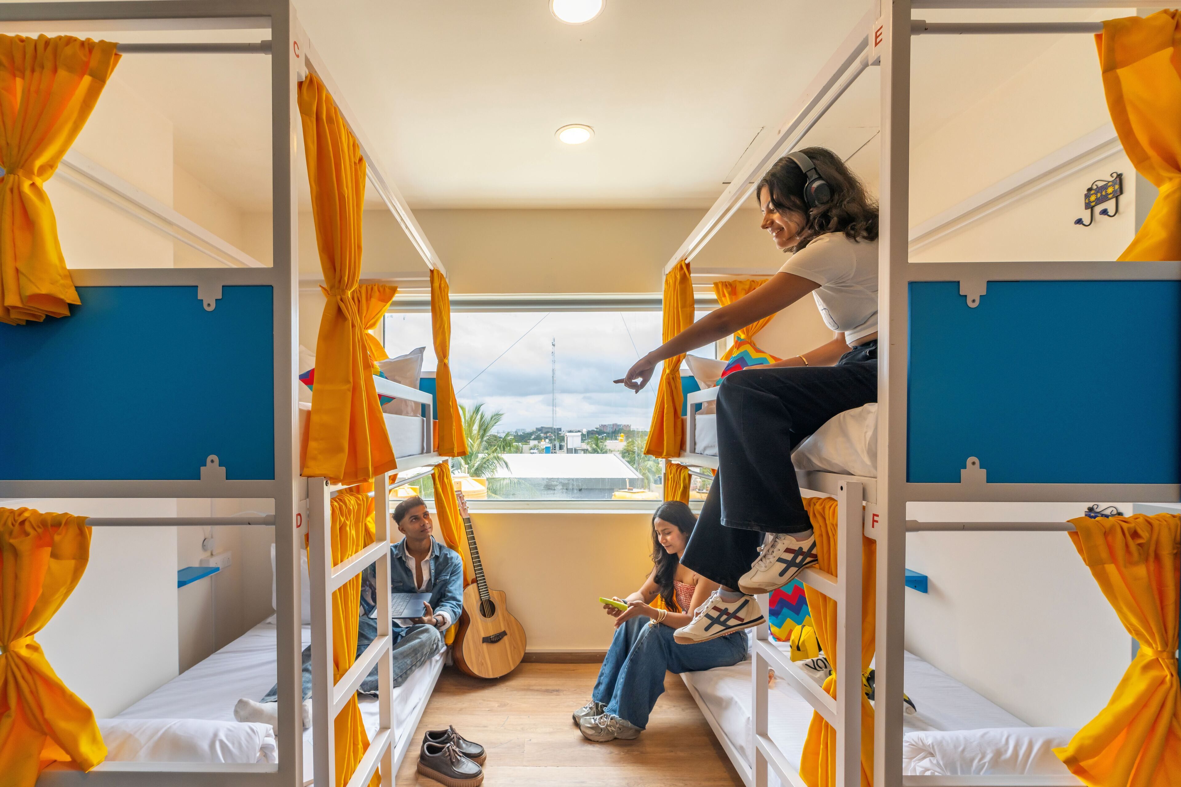 A dormitory room with bunk beds, a guitar, and a person using a tablet.