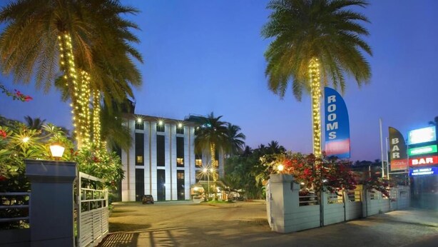 Ingresso di un hotel con facciata moderna, palme e insegne illuminate.